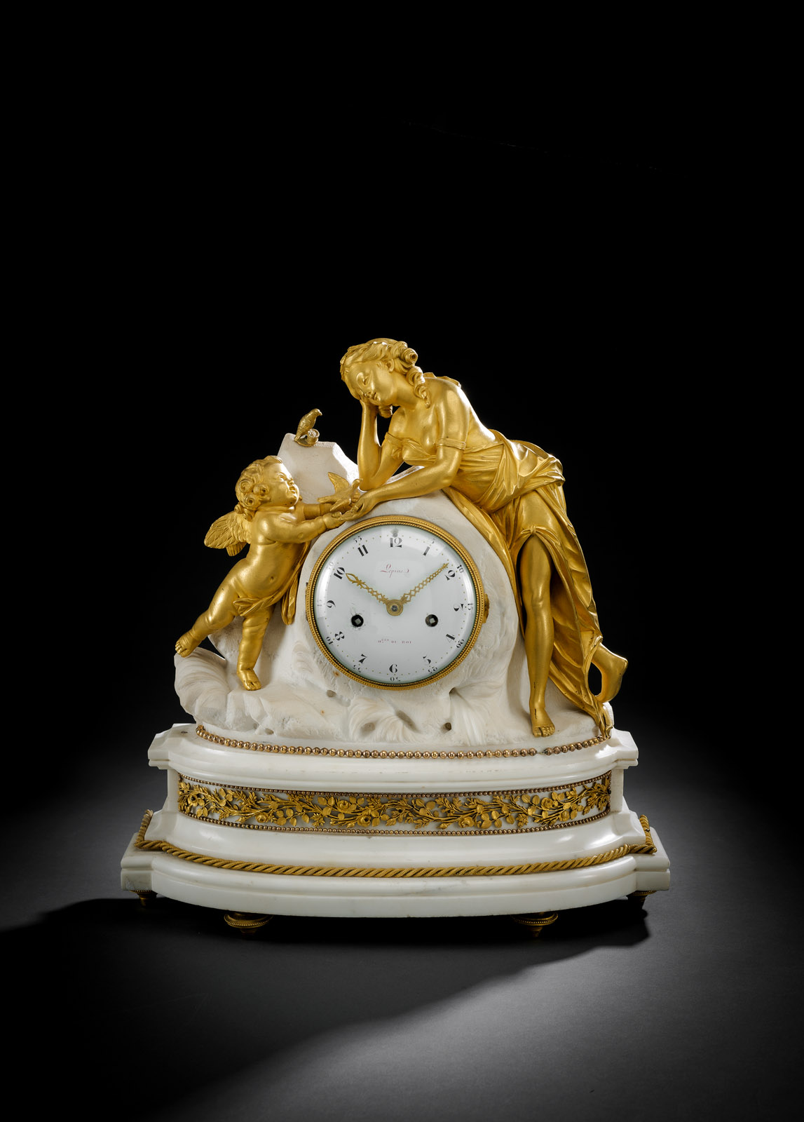 On a naturalized Carrara marble base, a fully plastic representation of Cupid and Psyche made of fire-gilded bronze, filigree base relief and disc feet. Bulged, white enamel dial with Arabic numerals and fine, ornate hands. Signed 