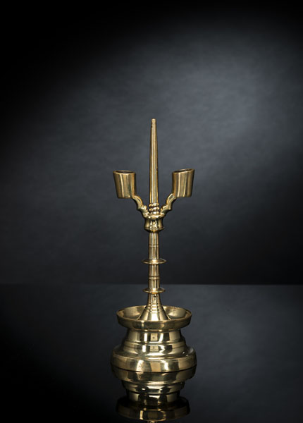 Polished brass candlestick with twin cylindrical sockets on scalloped, upturned arms, screw threaded over a central pricket above a blade knopped stem and domed base with drip bowl. Traces of age.
