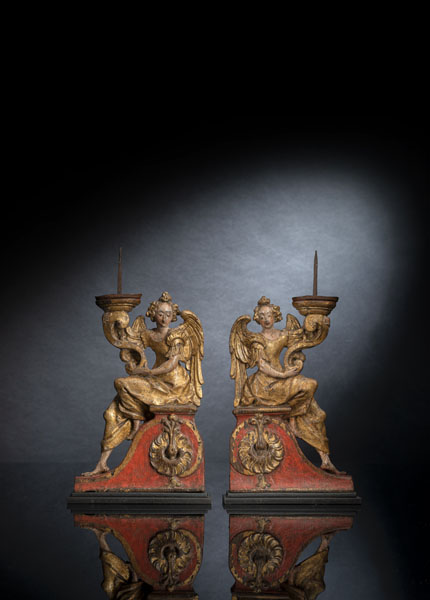 <b>Oakwood, worked in high relief from one piece. Volute shaped candlesticks with iron spikes, the angels sitting on pedestals decorated with ornaments. Remnants of the old polychromy, overpainted. Slight age damages. Upper part of the candlesticks added. On modern steel plinths.</b>