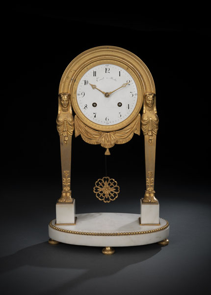 Oval white marble base and pedestals on bronze feet. Two karyatides holding the clockcase with drapery decor. White dial inscribed 