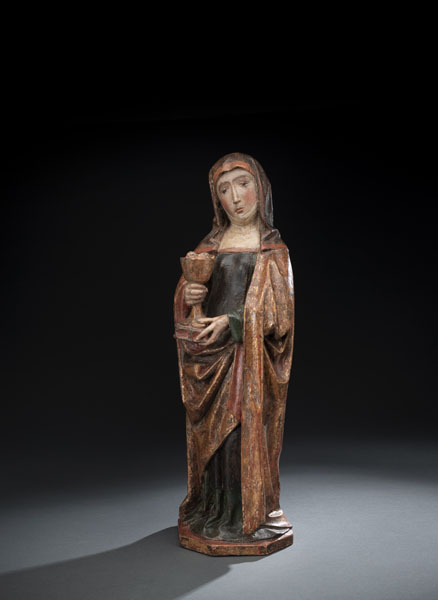 Standing Saint in her abbess robe with her attributes chalice and eyes. Hardwood, probably fruitwood, carved with hollowed back. Few remnants of the original polchromy, most of the old polychromy removed and later overpainted. Some restorations and damages due to age.