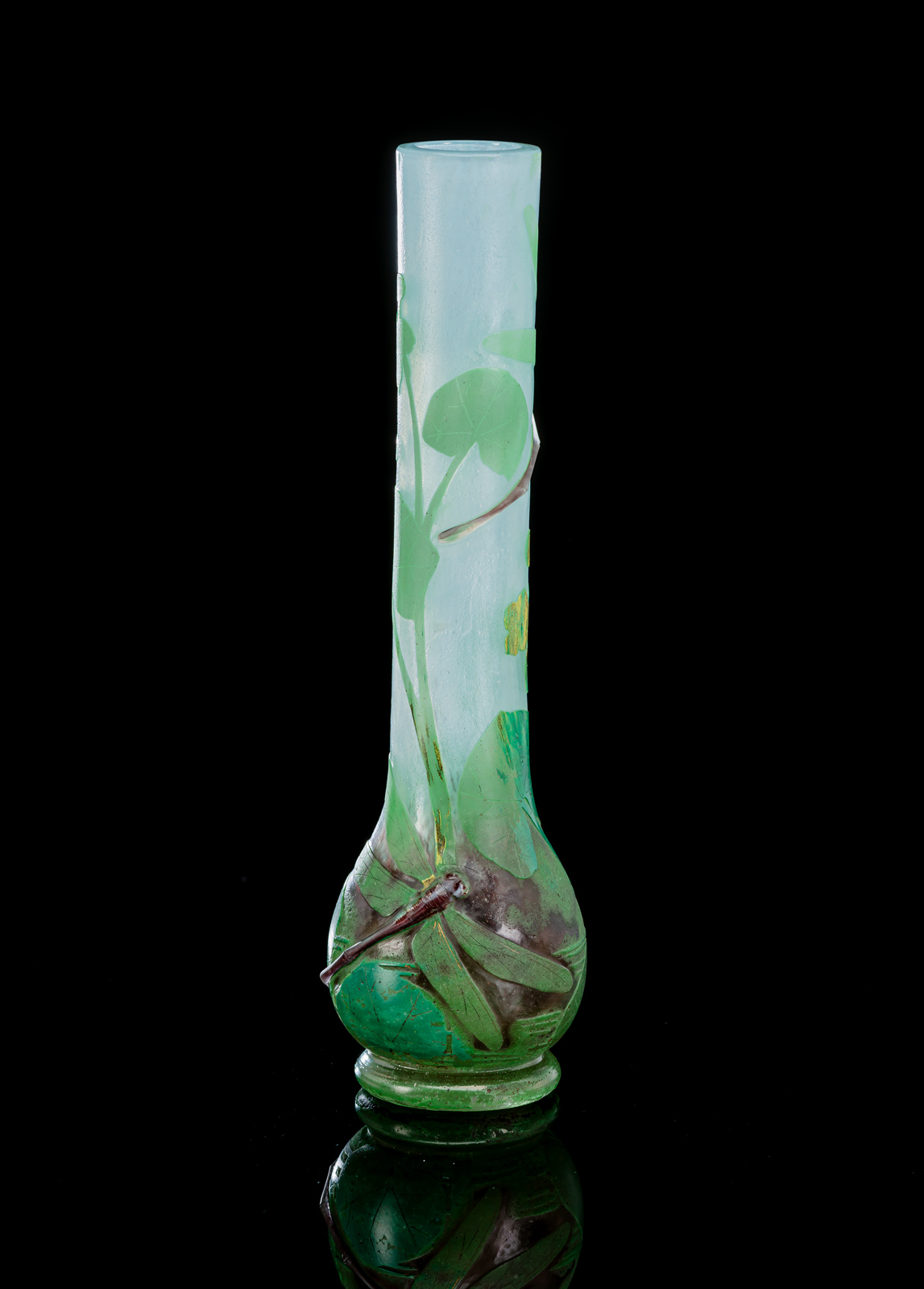 Farbloses Glas mit hellblauen, grünen und manganfarbenen Pulvereinschmelzungen, grün überfangen. Geätzter Dekor von Sumpfblumen, zwei aufgelegte Libellen. Am Boden Ritzsignatur 