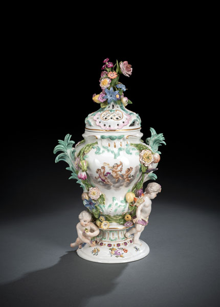 With applied flowers and putti, polychrome painted and gilt, partially openworked lid. Model by J.J. Kaendler. Blue crossed sword marks. Hairline cracks, minor losses and minute restorations.
