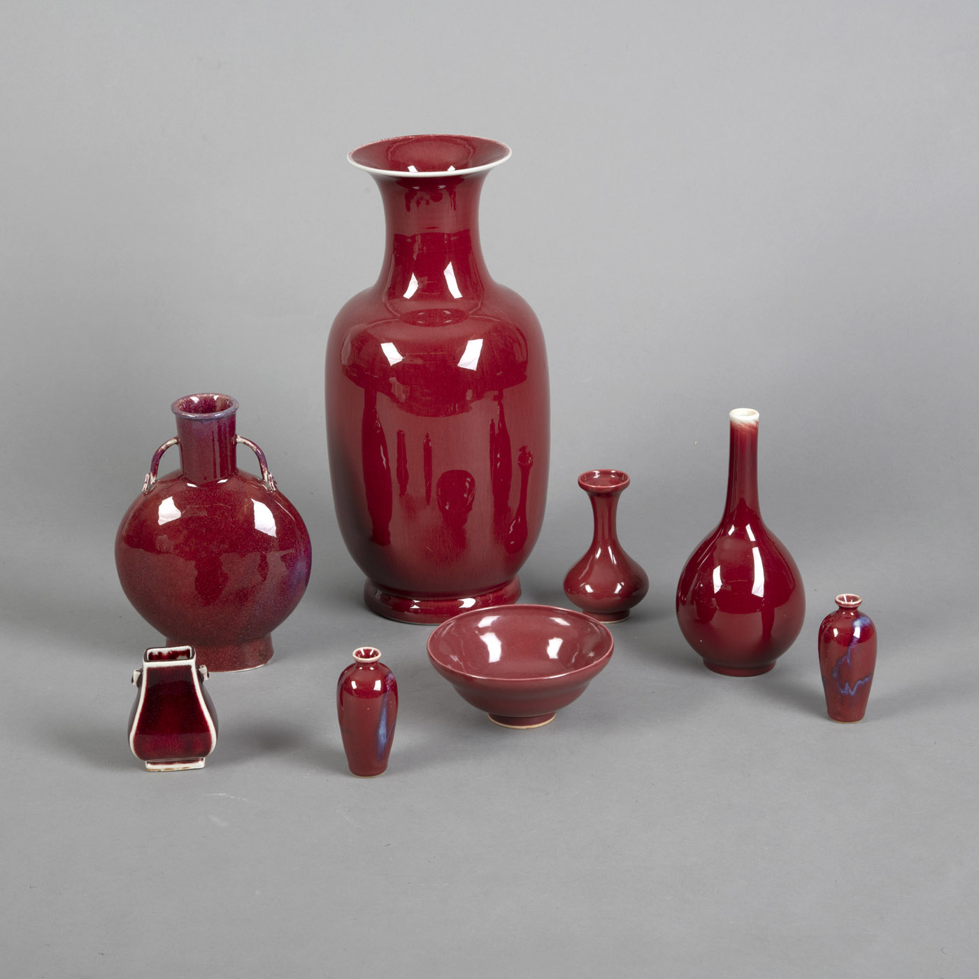 <b>Konvolut rot-glasiertes Porzellan, teils lavendelblau gefleckt: sieben Vasen und eine Schale</b>