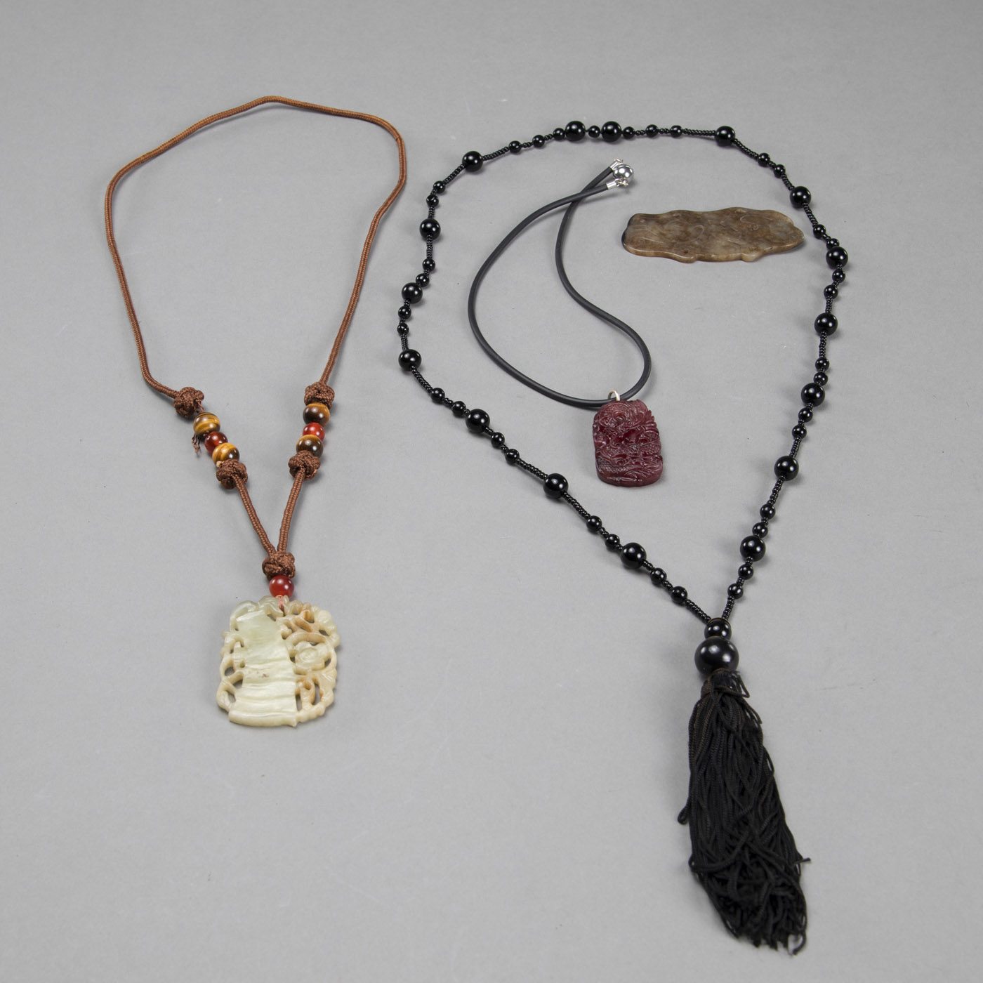 <b>THREE PENDANTS CARVED FROM JADE AND OTHER MATERIALS AND A CHAIN WITH BLACK BEADS</b>