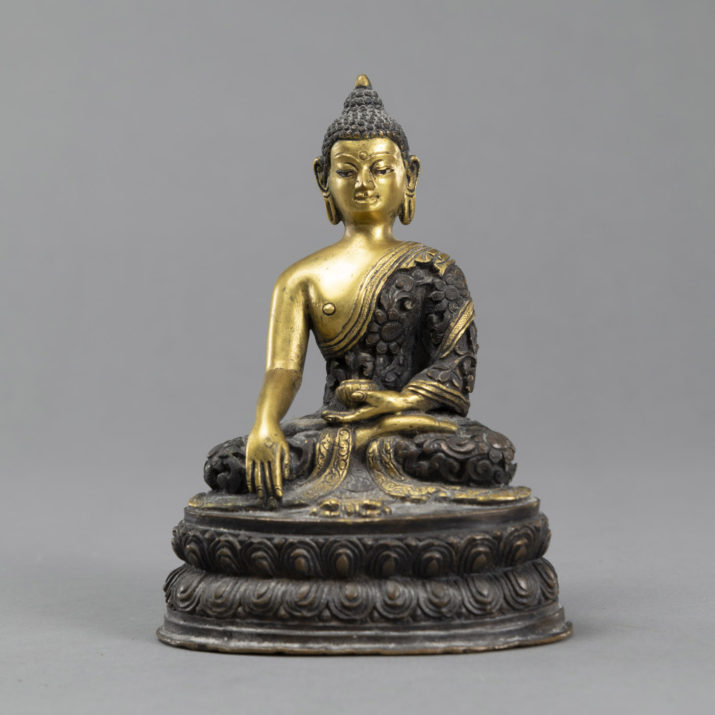 <b>A SEATED PARTLY GILD BRONZE BUDDHA AKSHOBHYA WITH AN ALMS BOWL AND WEARING A ROBE IN RELIEF</b>