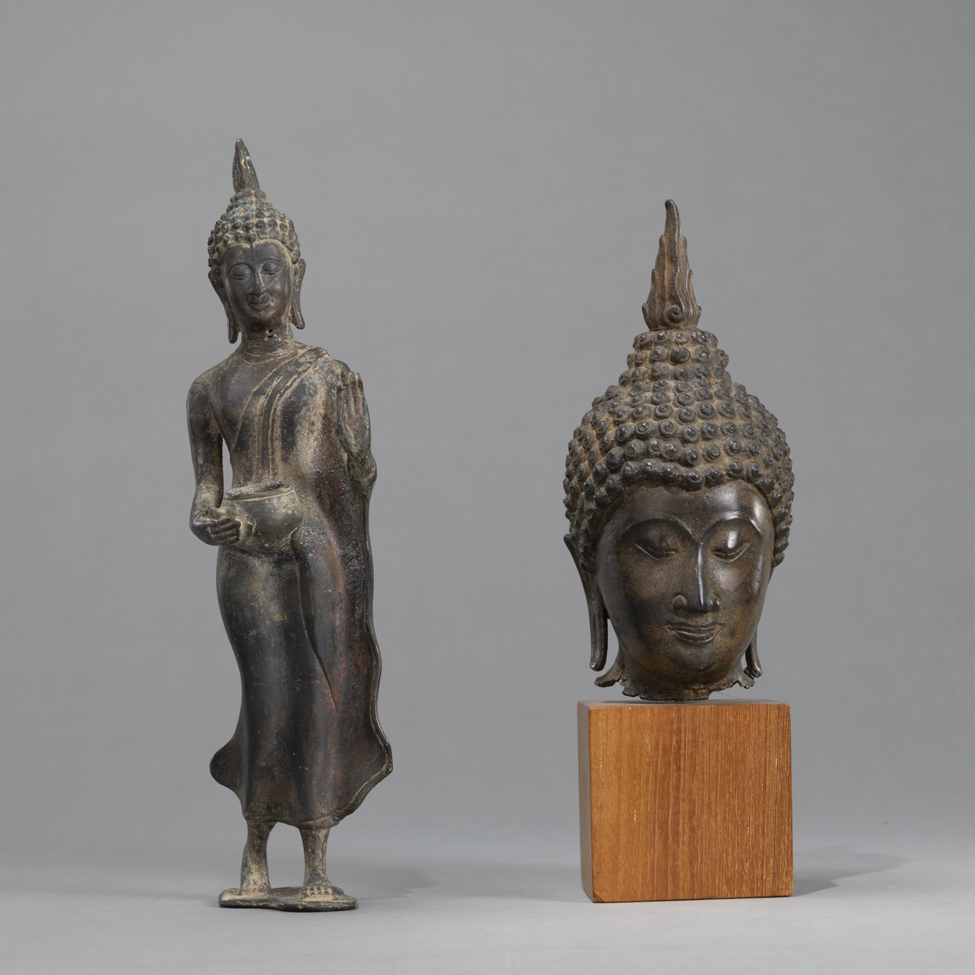 <b>A BRONZE BUDDHA HEAD MOUNTED ON A WOOD BASE AND A WALKING BUDDHA HOLDING A ALMS BOWL</b>