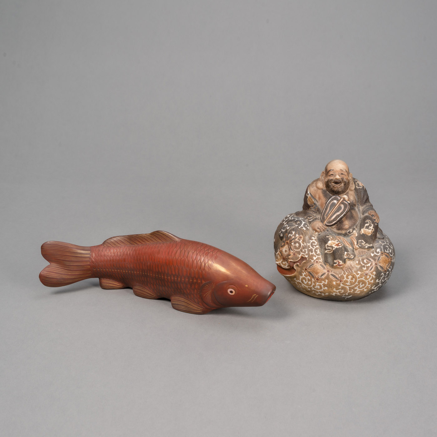 <b>Figur des Hotei aus Bizen-Ware und Okimono in Form eines Karpfens aus Holz mit Rot- und Goldlack gefasst</b>