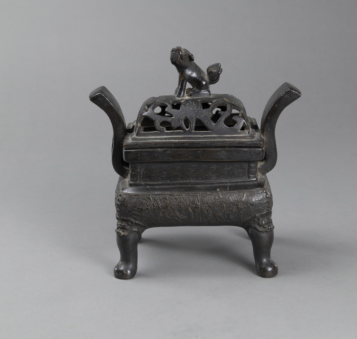 <b>A FOUR-FOOTED BRONZE INCENSE BURNER WITH TAOTIE MASK DECORATION AND A COVER IN OPENWORK AND CROWNED BY A SEATED LION</b>
