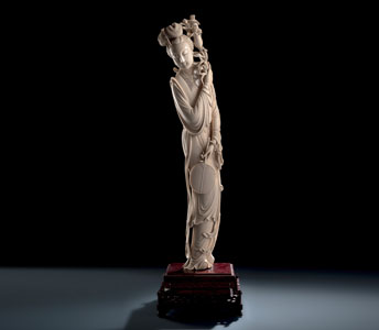 <b>A FINE AND LARGE IVORY MODEL OF A STANDING BEAUTY WITH LILIES AND A FAN, MOUNTED ON A WOOD STAND</b>