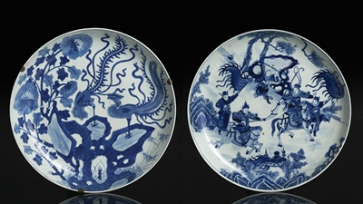 <b>Zwei unterglasurblau dekorierte große Teller mit Romanszene bzw. Phönixpaar auf Felsen</b> <b>Zwei unterglasurblau dekorierte große Teller mit Romanszene bzw. Phönixpaar auf Felsen</b>