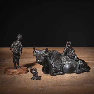 <b>Drei Okimono aus Bronze: ruhender Büffel mit jungem Hirten auf Rücken, stehende Bäuerin und sitzender Knabe mit erhobenem Arm</b>
