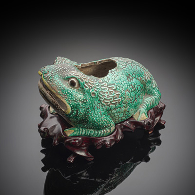 <b>Pinselwascher in Form einer dreibeinigen Kröte aus Bisquit-Porzellan mit grün-gelber Glasur, Holzstand</b>