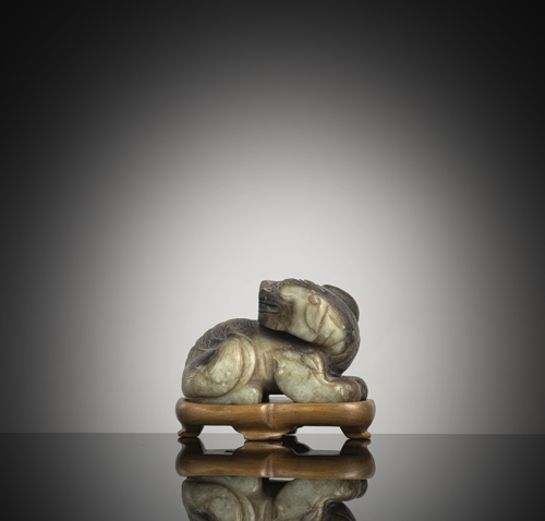 <b>A recumbent green-brown jade model of a mythical creature on a wooden stand</b>