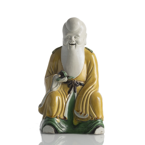 <b>A three-coloured glazed biscuit porcelain figure of Shoulao, holding a peach in his right hand, shown seated</b>