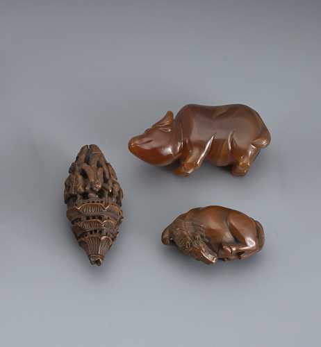 <b>Two carved nut toggles: a reclining horse and a pagoda with figures, and an agate carving of a buffalo</b>