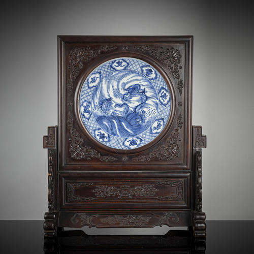 <b>A carved wood tabel screen inlaid with a round underglaze blue glazed porcelain tile with fish and dragon decoration</b> <b>A carved wood tabel screen inlaid with a round underglaze blue glazed porcelain tile with fish and dragon decoration</b>