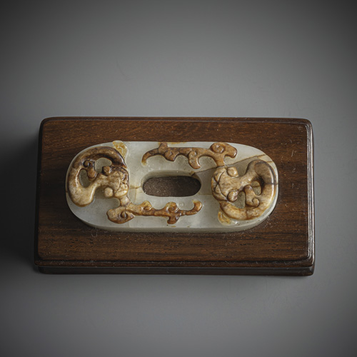 <b>A carving of an oval clasp made of almost white jade with chilong in relief in caramel-coloured tones mounted on a wooden stand</b>