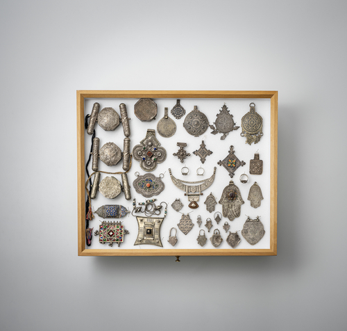 <b>Gruppe von Schmuckstücken, Amulett-Dosen, Anhänger und Kettschmuck, teils in Silber gearbeitet, in zwei Glaskästen montiert</b> <b>Gruppe von Schmuckstücken, Amulett-Dosen, Anhänger und Kettschmuck, teils in Silber gearbeitet, in zwei Glaskästen montiert</b>