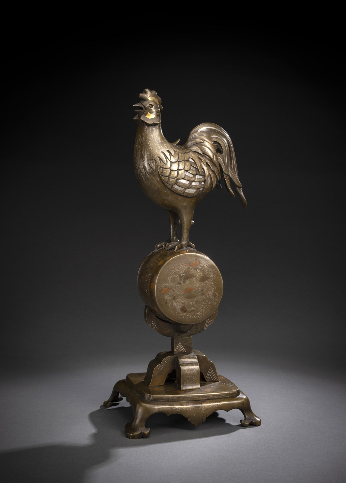 <b>A BRONZE KORO IN SHAPE OF A COCKEREL PERCHED ON A DRUM INLAID WITH GOLD, COPPER AND SILVER</b>