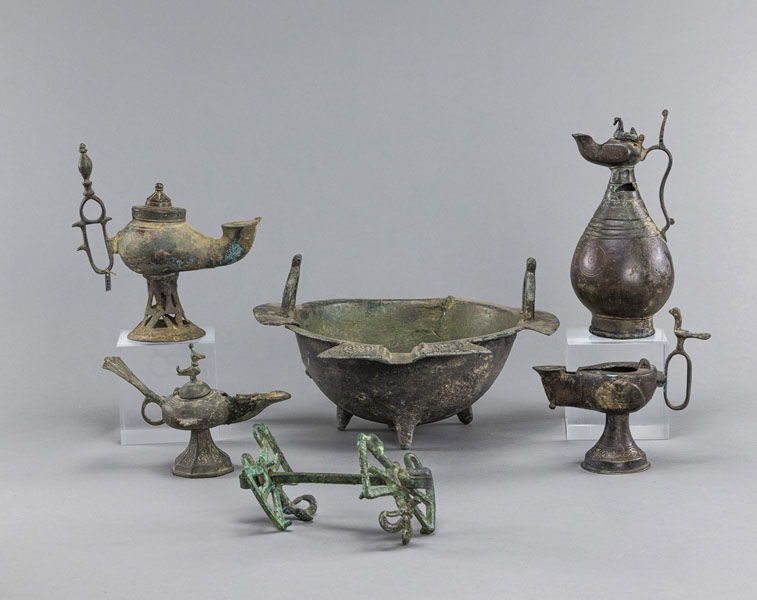 <b>Gruppe von sechs Bronzearbeiten, u.a. ein Becken, drei Öllampen, eine Kanne und eine Trense. Partiell ornamental graviert.</b>